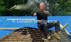 A 21st Century roofer sheds tiles from a mid-20th Century north London bungalow. © Paul Coleman, London Intelligence ®